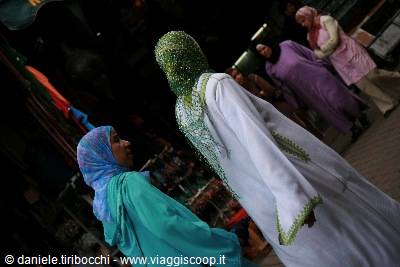 Veiled women walk past market stalls, one in a green embroidered white dress