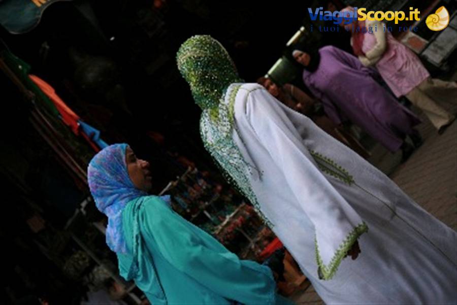 Veiled women walk past market stalls, one in a green embroidered white dress