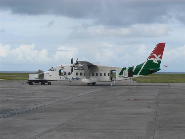 Air Seychelles twin-propeller plane parked on tarmac, door open, cloudy sky