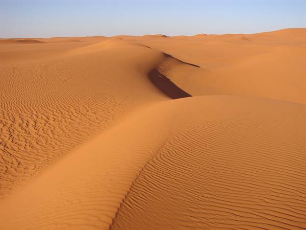 Orange sand dunes with wind ripples, sharp shadows under a clear blue sky