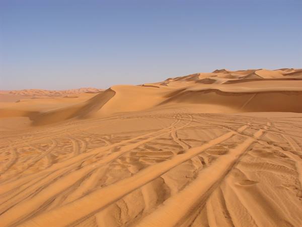 Tire tracks on orange sand between desert dunes under a blue sky