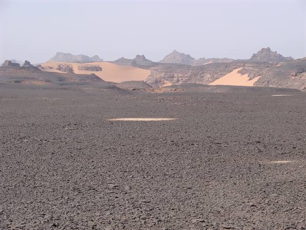 Rocky black stone desert with pale sand dunes between mountains