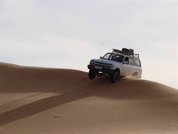 White off-road vehicle loaded with luggage descends a sand dune