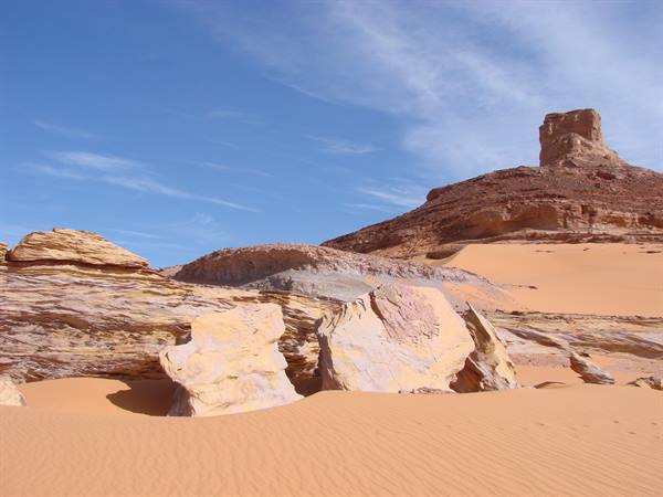 Light rocks among sandy dunes, rocky mountain and blue sky in the desert
