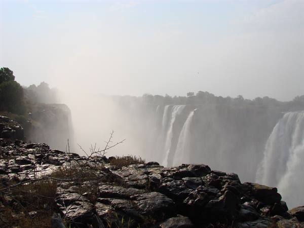 Victoria Falls: waterfalls shrouded in mist, wet black rocks in foreground