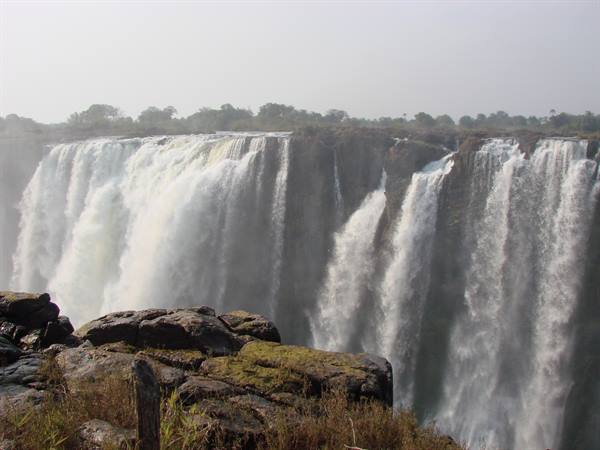 Victoria Falls: mighty foamy cascades over basalt rocks under hazy light