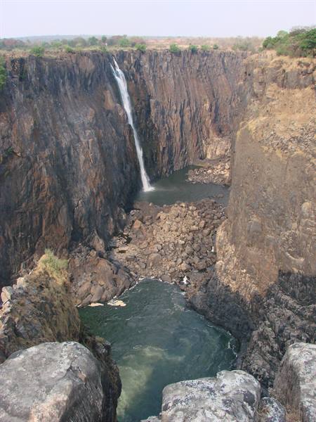 Waterfall plunging into basalt gorge with green river below, Victoria Falls