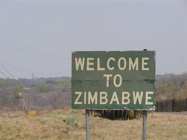 Green sign reading Welcome to Zimbabwe along a road amid dry grass