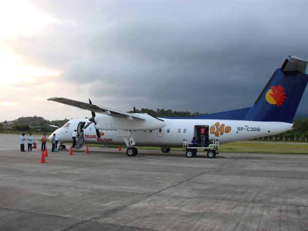 Seair Dash 8 turboprop on tarmac, passengers boarding via stairs, cloudy sky