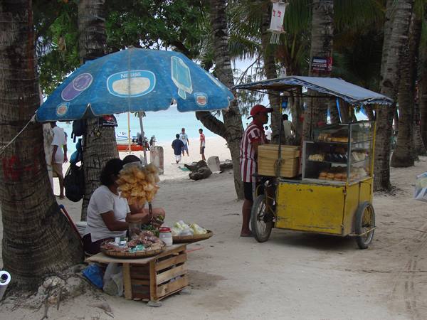 Vendor under blue umbrella and yellow food cart on Boracay beach