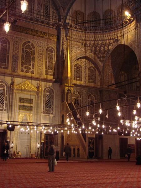 Inside Istanbul's Blue Mosque, low-hanging lamps, gilded minbar, worshippers on red carpet