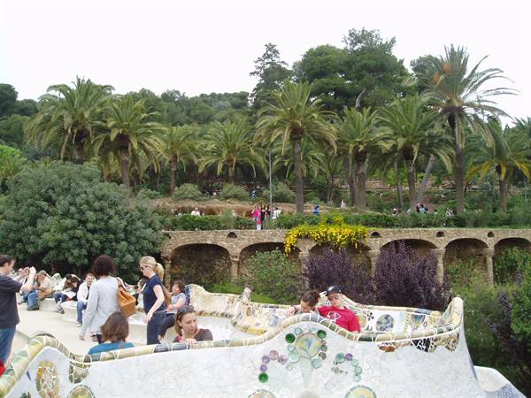 Tourists on the mosaic terrace of Park Güell, among palms and stone arches