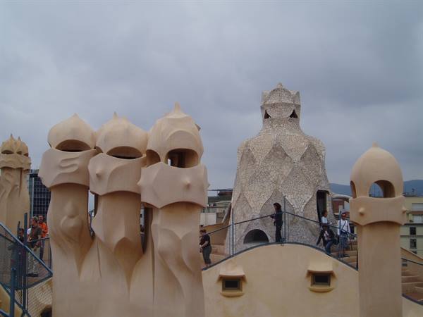 Gaudí's stone chimneys on Casa Milà rooftop, visitors under grey sky