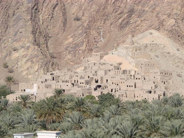 Mud-brick village under arid rocky mountains, green palm grove in front