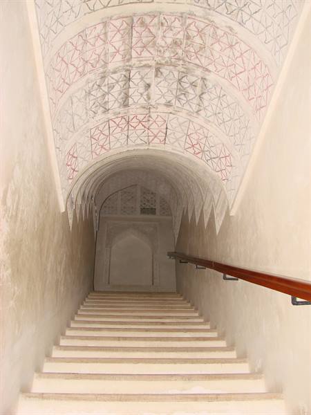 Stone staircase under a vault painted with red geometric patterns, wooden handrail