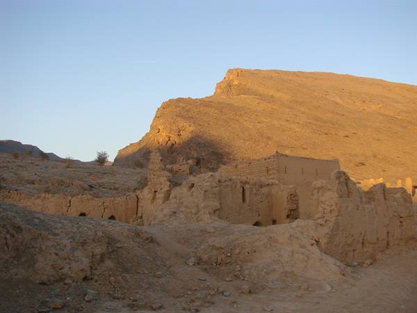 Mud-brick village ruins beneath a golden desert mountain at dusk