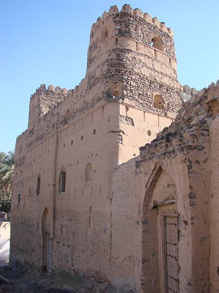 Ancient mud-brick fort with crenellated tower, bright desert sunlight