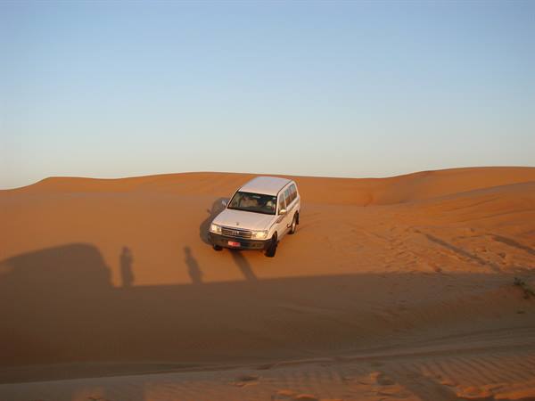 White 4x4 descending a golden sand dune