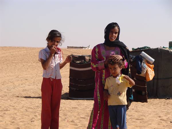 Woman and children in front of tents on sandy desert ground