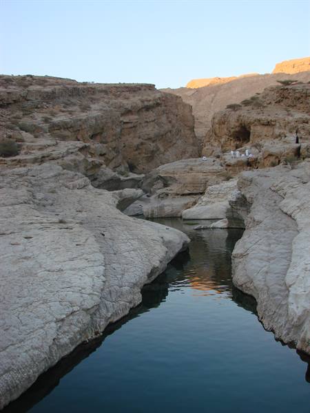 Calm pool between eroded limestone rocks in a wadi under blue sky