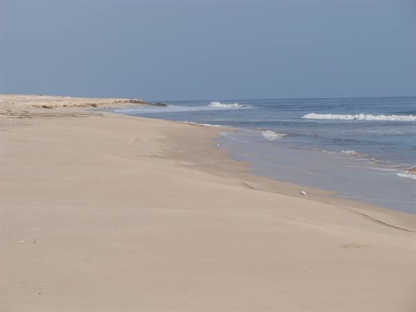 Pale sand and small waves along an empty beach under a blue sky