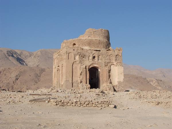 Ancient mud-brick mausoleum, partially collapsed, among arid rocky desert mountains