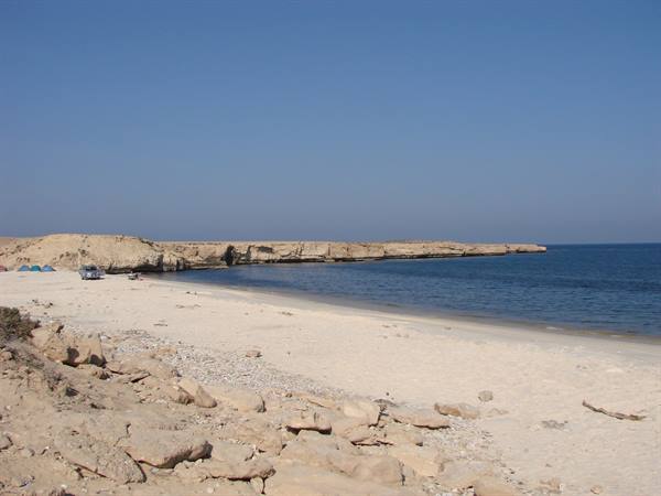 White sand beach with rocky cliffs, tents and a car under clear sky