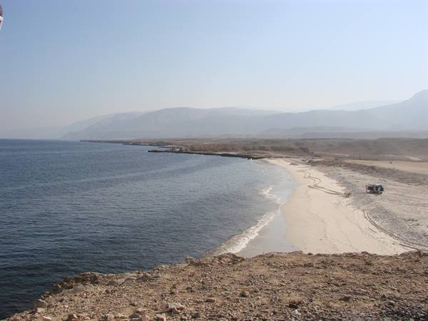 Sandy beach with parked car, arid rocky cliffs and hazy mountains
