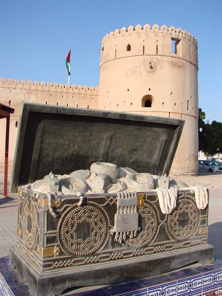 Ornate metal treasure chest sculpture before Nizwa Fort's round tower, daylight