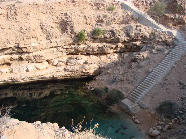 Concrete staircase descends to turquoise water of Bimmah sinkhole among arid rocks