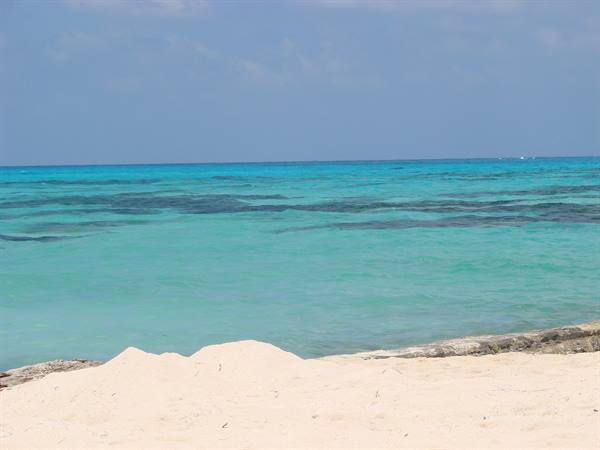 White sand and rocks before a turquoise sea under a blue sky