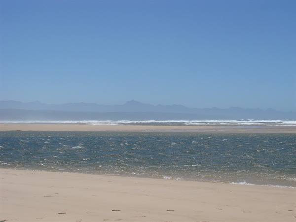 Waves on golden sand, hazy mountains on the horizon, blue sky