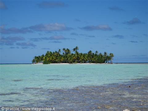Small palm-covered islet in a turquoise lagoon with white sand and blue sky