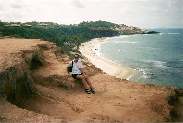 Woman sitting on red sand cliff above beach and ocean, Praia da Pipa