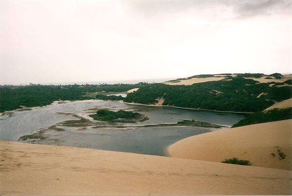 Golden sand dunes above a lagoon surrounded by green vegetation, cloudy sky
