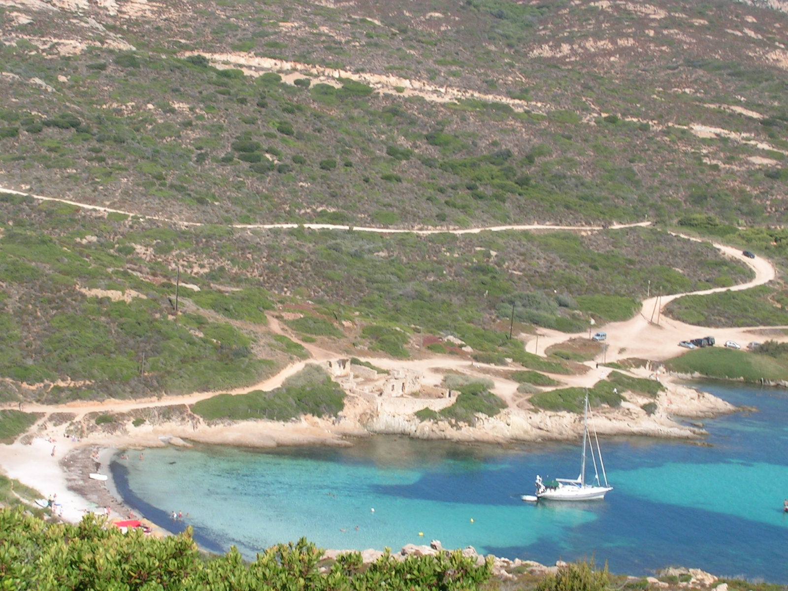 Sailboat anchored in turquoise cove, dirt paths through Mediterranean scrub and granite