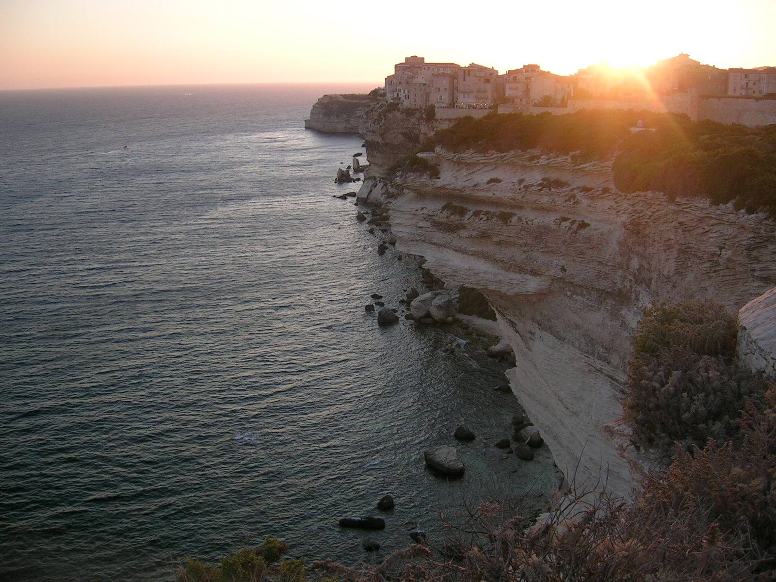 Houses atop Bonifacio limestone cliffs at sunset over the sea