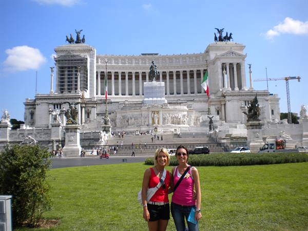 Two tourists smiling in front of the Vittoriano monument in Rome on a sunny day