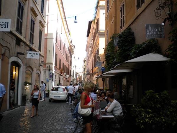 Cobblestone street with people at wine bar tables among ochre buildings