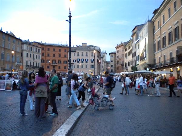 Crowd of tourists on cobblestones in Piazza Navona, Rome, pastel buildings at dusk