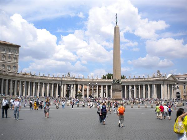 Tourists walk across St. Peter's Square between the obelisk and the colonnade