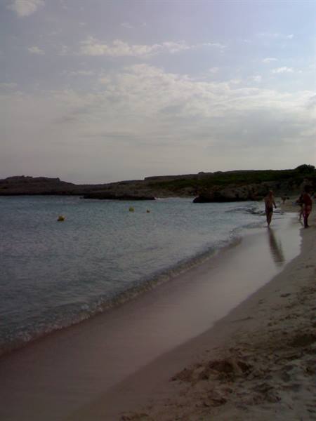 Bathers on wet sand of a beach with rocky shore and yellow buoys