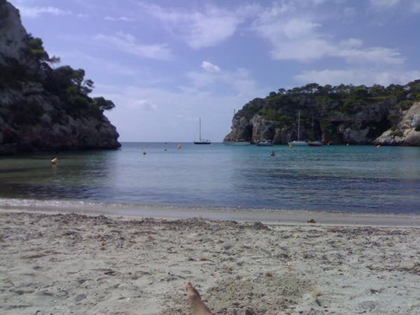 Cala Macarella: white sand beach, sailboats anchored between green rocky cliffs