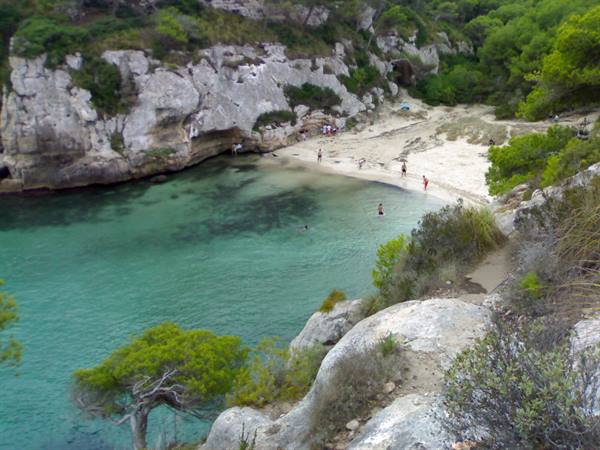 Cala Macarella: white sandy beach between limestone rocks and pines, swimmers in turquoise water