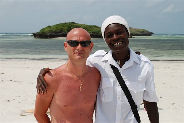 Two men embrace on white sand beach, green island over turquoise sea