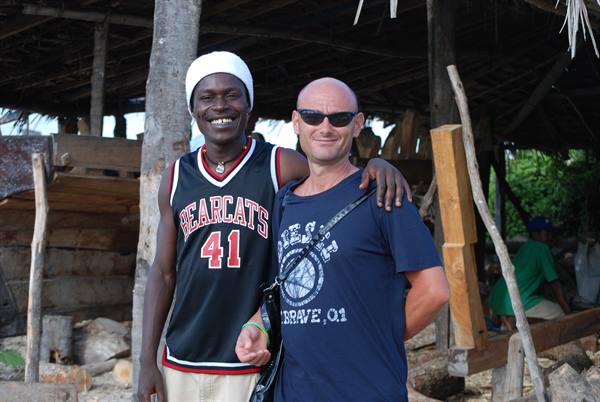 Tourist arm in arm with smiling friend in black jersey, under wooden shack