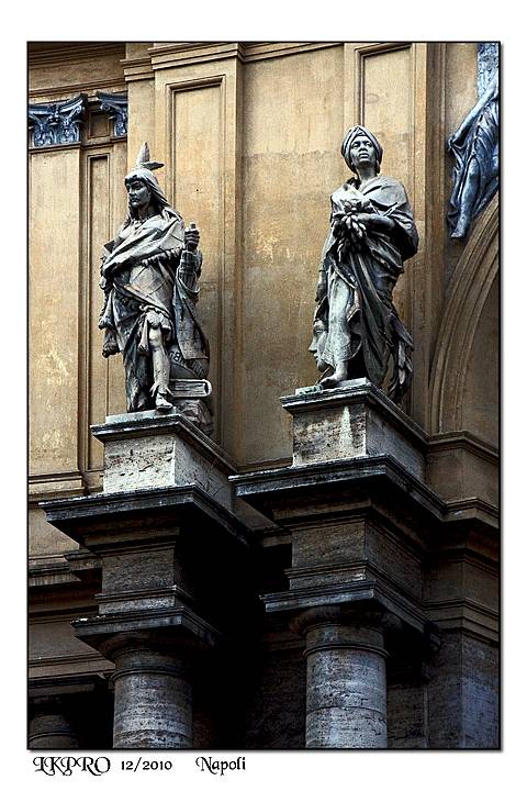Two stone statues on columns of a Baroque facade in Naples