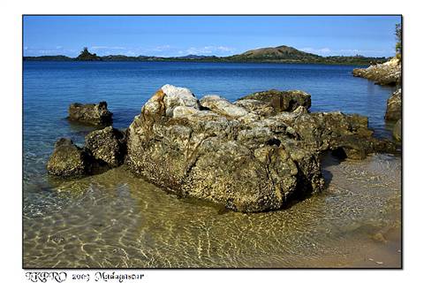 Sunlit rocks in clear shallow water, green hills across the bay, Madagascar