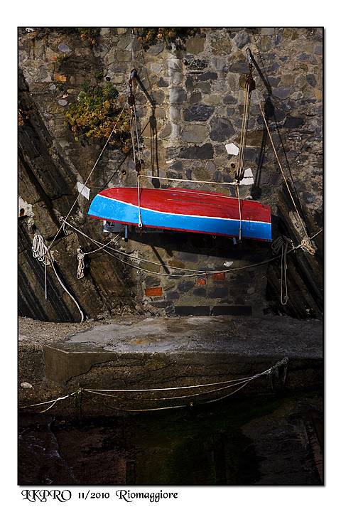 Red and blue boat hoisted on ropes against the stone wall, Riomaggiore