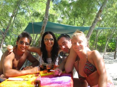 Four smiling friends at a table in a beachside bar
